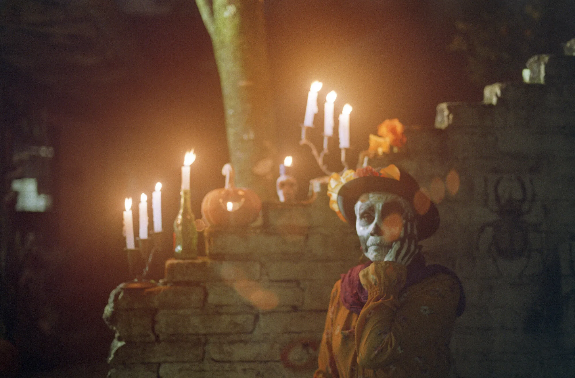 La misma catrina, ahora mirando a la cámara con la mano en la mejilla, entre velas encendidas.